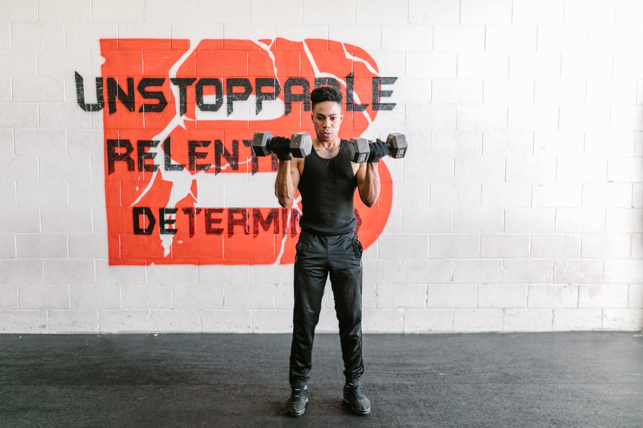 hero-img-02 Focused man lifts dumbbells with determination in a gym against motivational graffiti